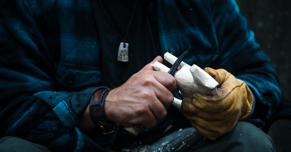 man whittling wood in the forest